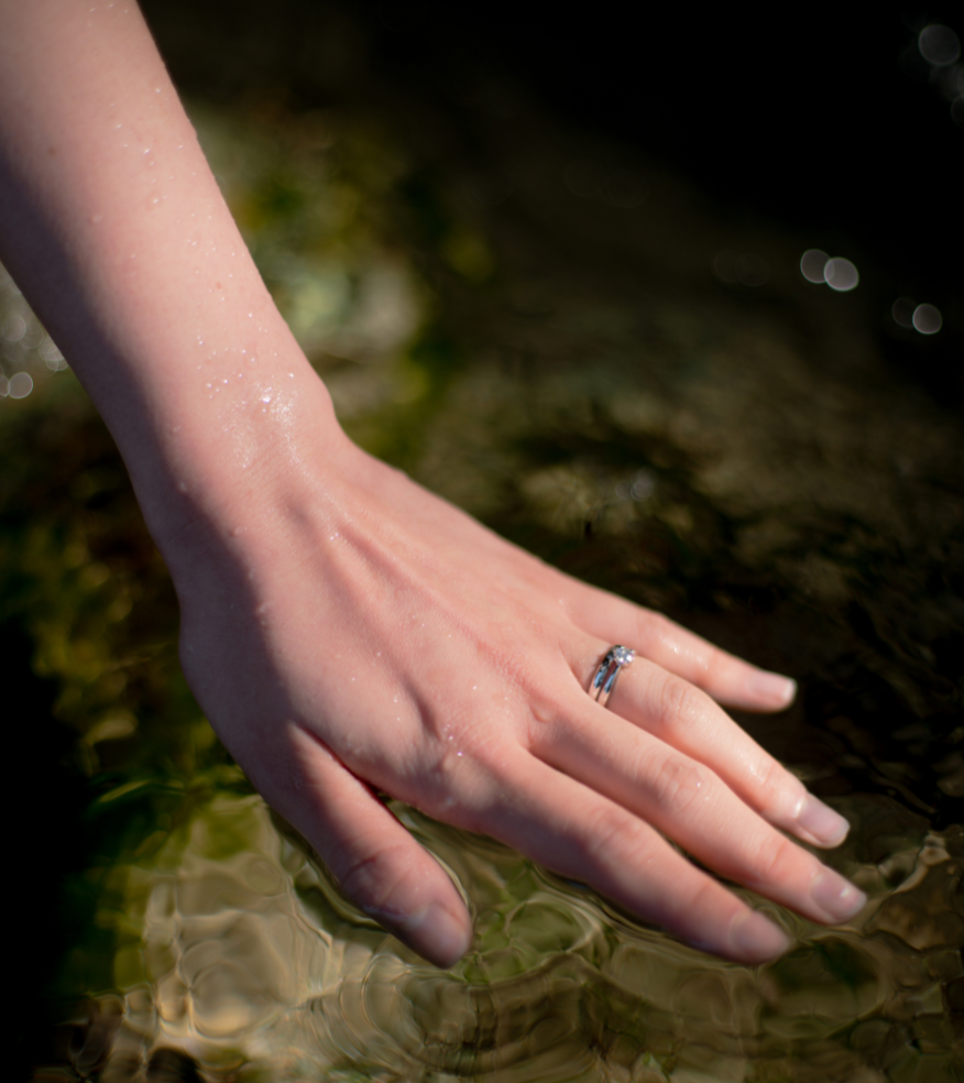 水面に添える手に輝く結婚指輪と婚約指輪　沖縄ミンサー模様　琉球杢目