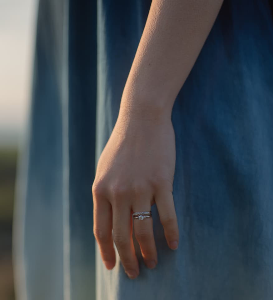 女性の左手に輝く沖縄ミンサー模様が施された婚約指輪と結婚指輪　琉球杢目　